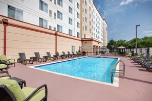 A hotel pool area with lounge chairs and a basketball court.