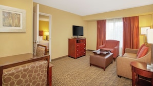 Habitación de hotel con cama, escritorio con silla, sofá, televisor sobre un mueble bajo y una mesita.