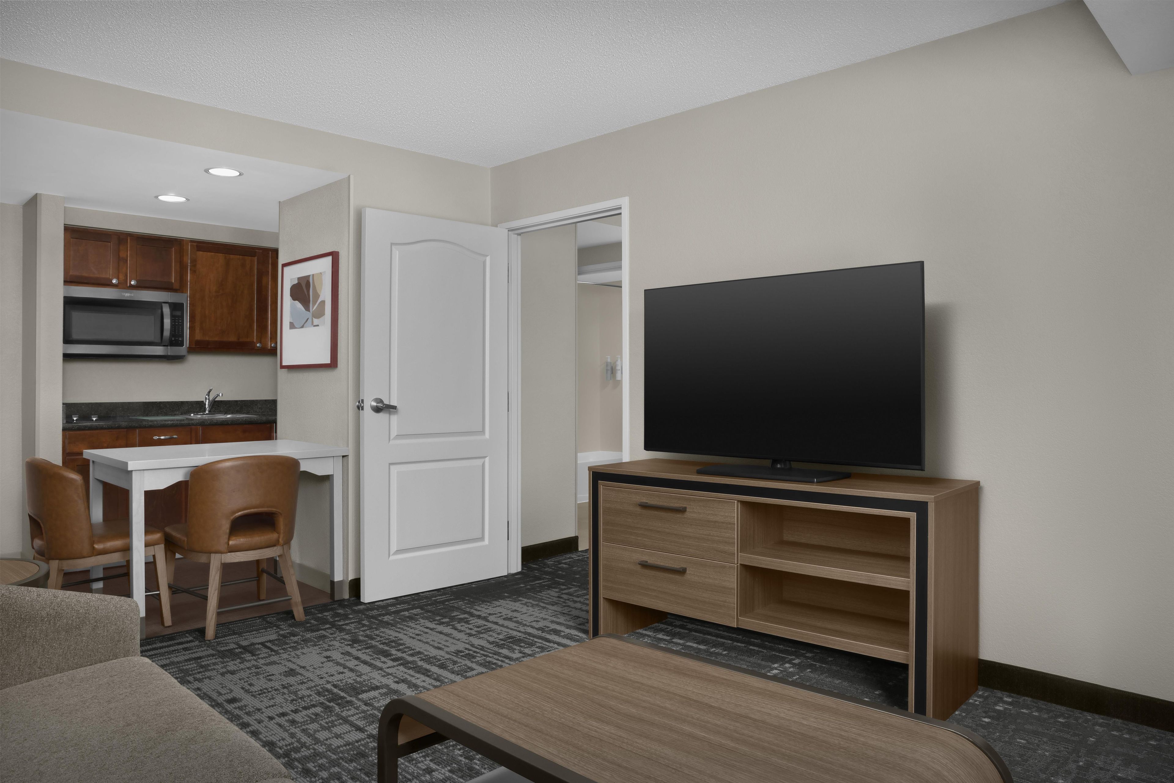 Een hotelkamer met een kitchenette, een televisie, een bureau en een stoel.