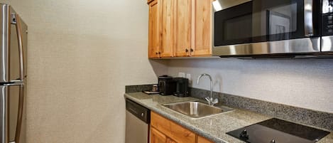 A kitchen with wooden cabinets, a stainless steel refrigerator, a microwave, a sink, and a dishwasher.