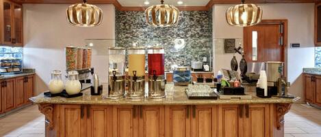A spacious kitchen with wooden cabinets, a granite countertop, and hanging pendant lights.