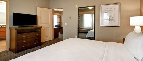 A hotel room with a large bed, a flat-screen TV on a wooden dresser, a bedside lamp, and a framed picture on the wall.