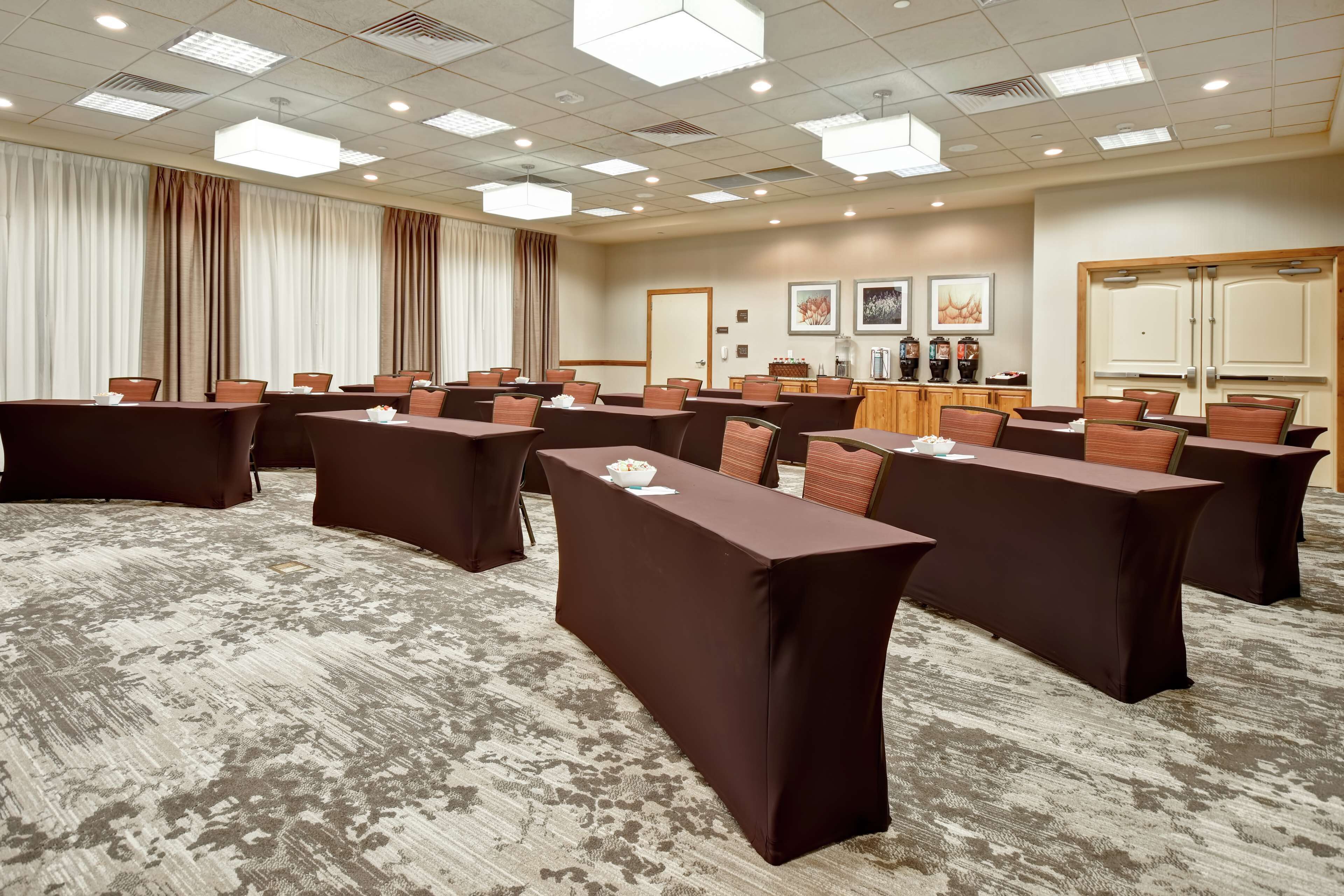 A conference room with multiple tables and chairs, a carpeted floor, and a ceiling with recessed lighting.