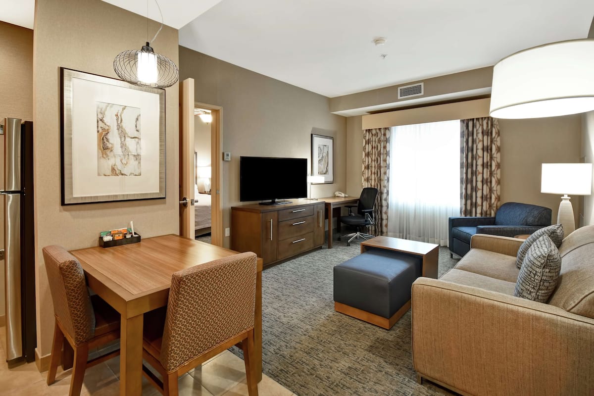 Een hotelkamer met een eettafel, stoelen, een bank, een televisie, een bureau en een lamp.