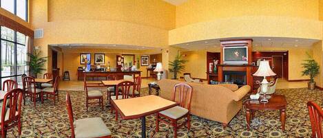 A spacious lobby with a high ceiling, a fireplace, and a television. There are multiple seating areas with chairs and tables.