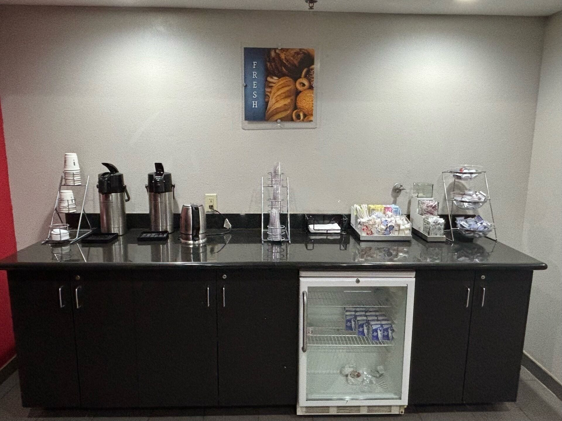 A hotel reception area with a refrigerator, coffee maker, and various amenities on the counter.