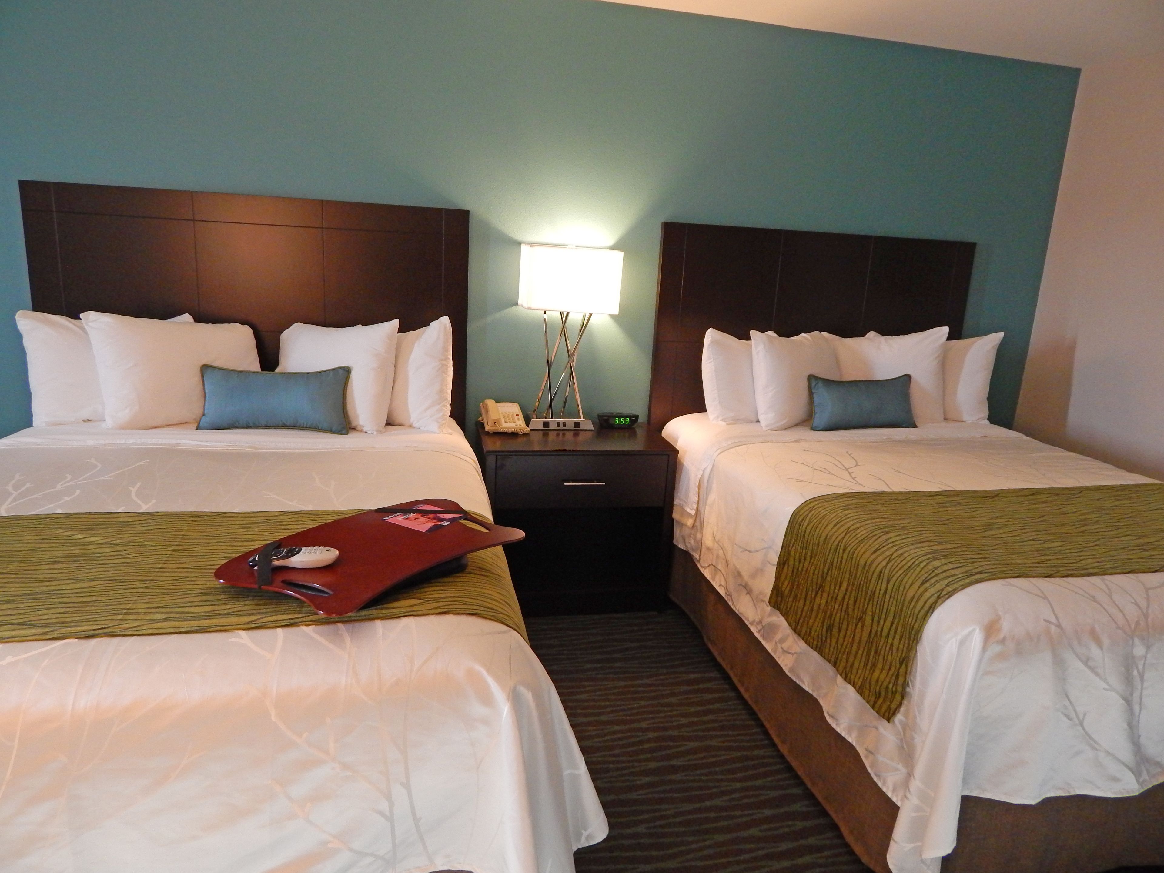 Habitación de hotel con dos camas, una mesita de noche, una lámpara y una bandeja roja con un control remoto.
