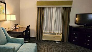 A hotel room with a single bed, a desk with a chair, a television, and an air conditioning unit.