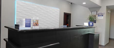 A reception desk with a modern design, including a textured wall and a blue-lit panel. There are informational brochures and a sign indicating a service promise.