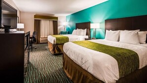 Habitación de hotel con dos camas, un escritorio con televisor y un ventanal con cortinas.