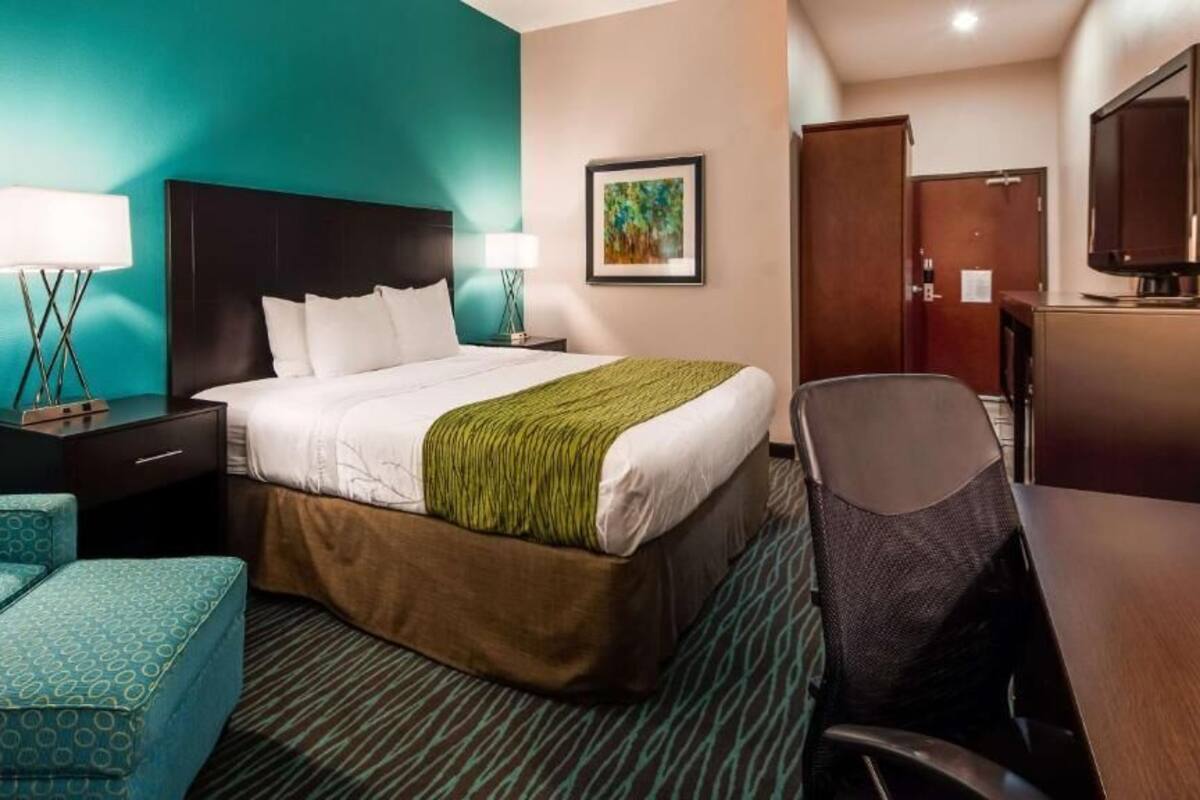 Una habitación de hotel con una cama, dos sillas, un escritorio, un televisor y una puerta.