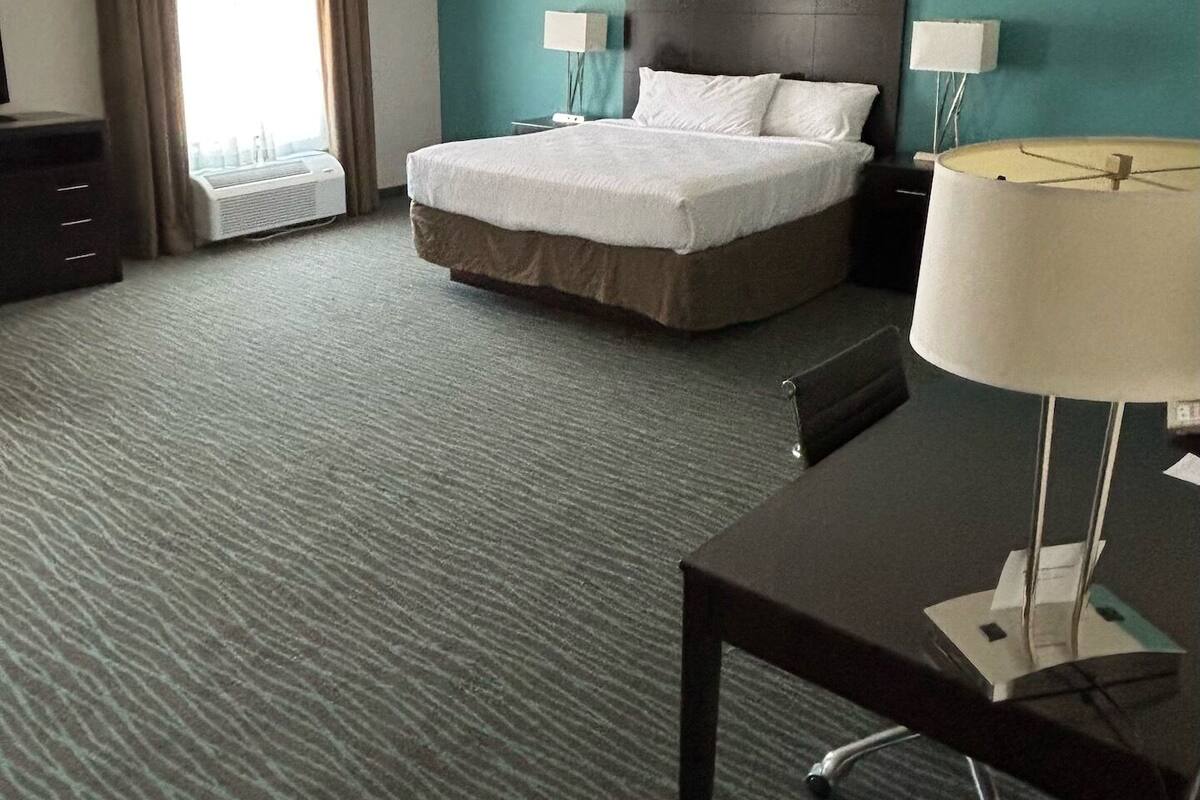 Habitación de hotel con cama, dos lámparas de noche, un escritorio y una ventana con cortinas.