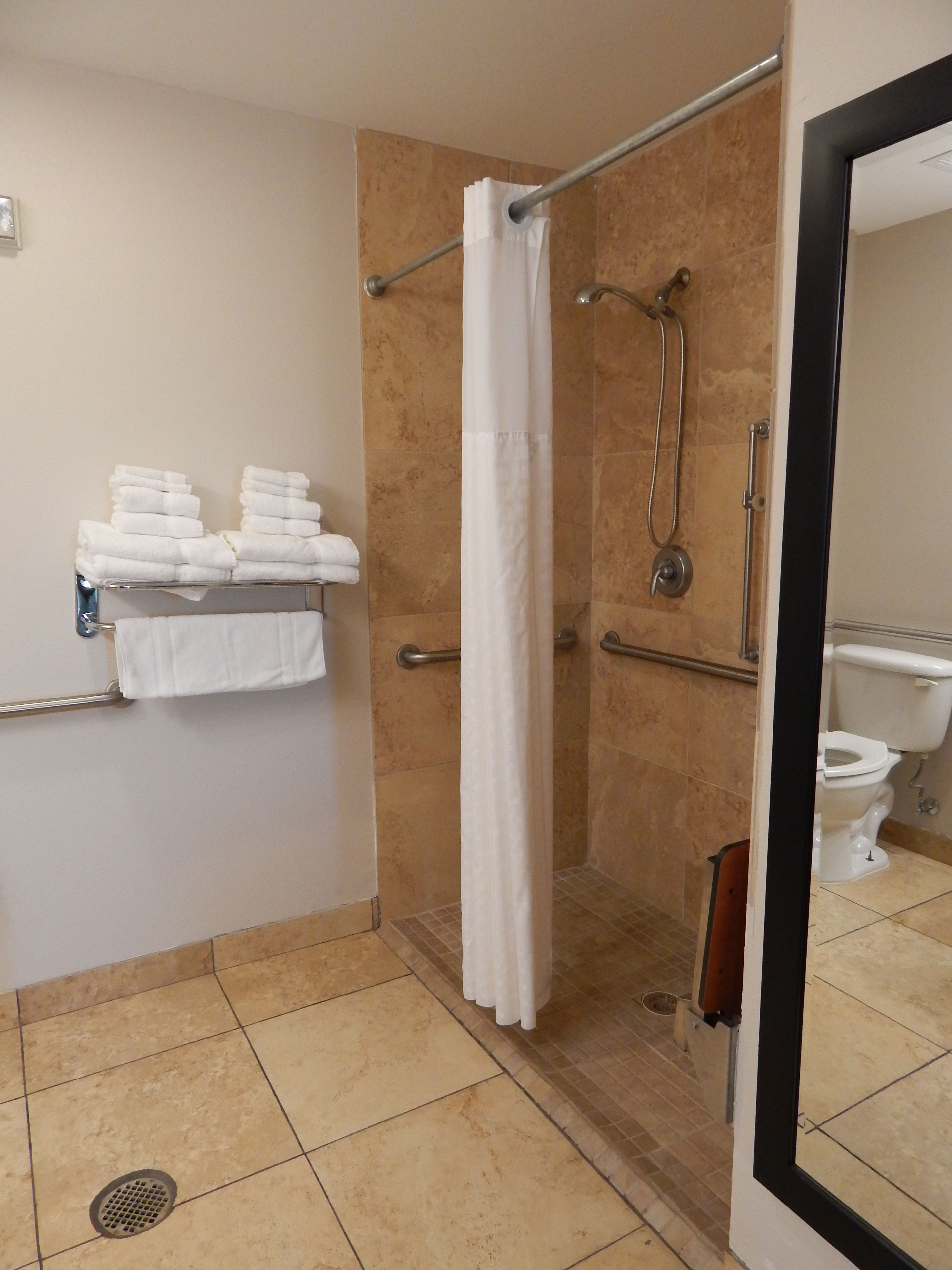 A bathroom with a shower, a toilet, and a towel rack with folded towels.