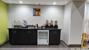 Una estación de desayuno autoservicio con un refrigerador, máquinas de café y dispensadores de condimentos.
