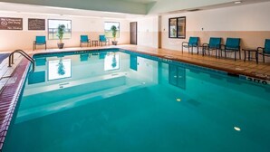 Una piscina interior con un letrero que indica que no hay salvavidas de servicio, sillas y plantas en macetas.