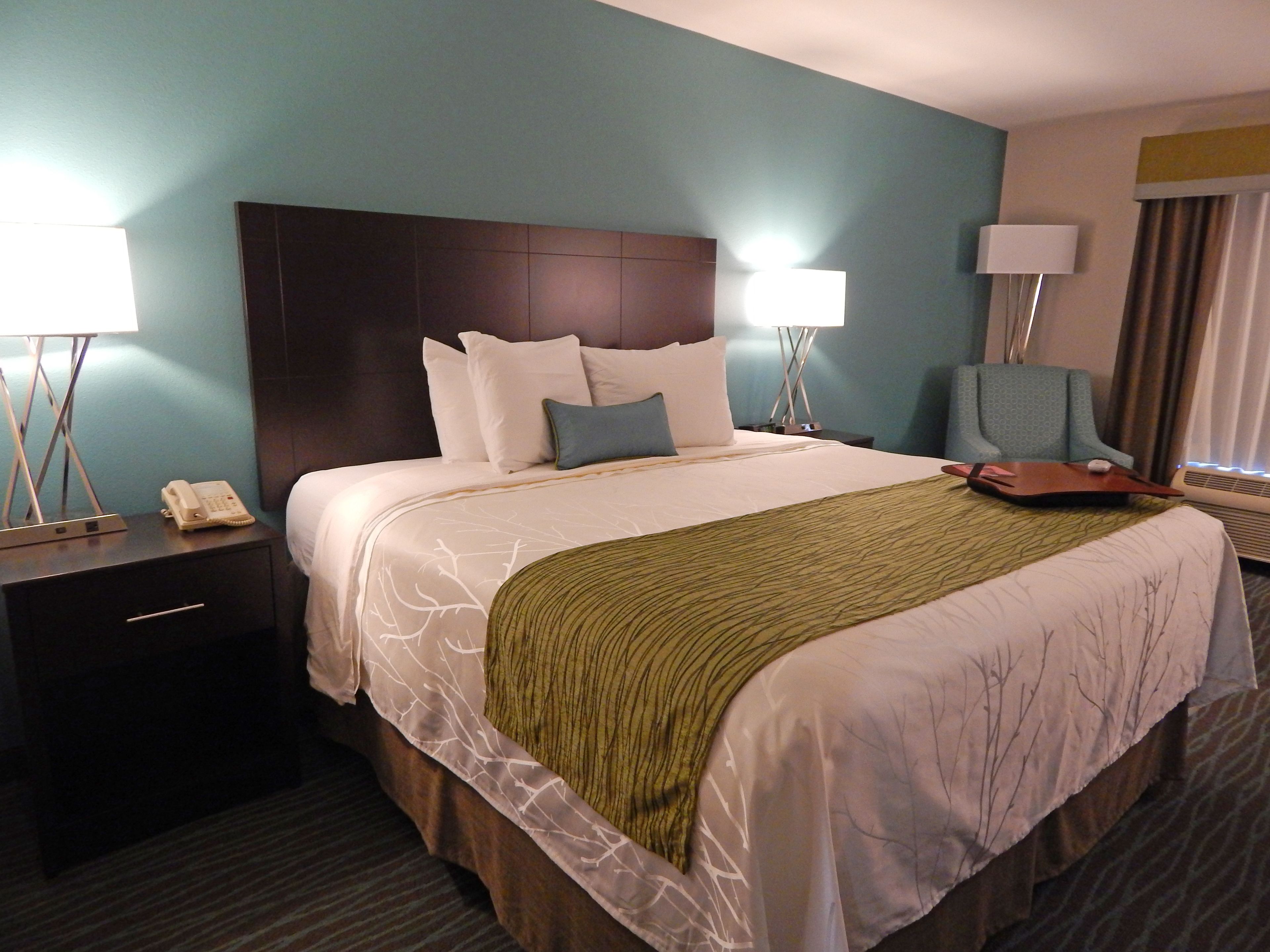 A hotel room with a large bed, a nightstand with a phone, a chair, and a lamp.