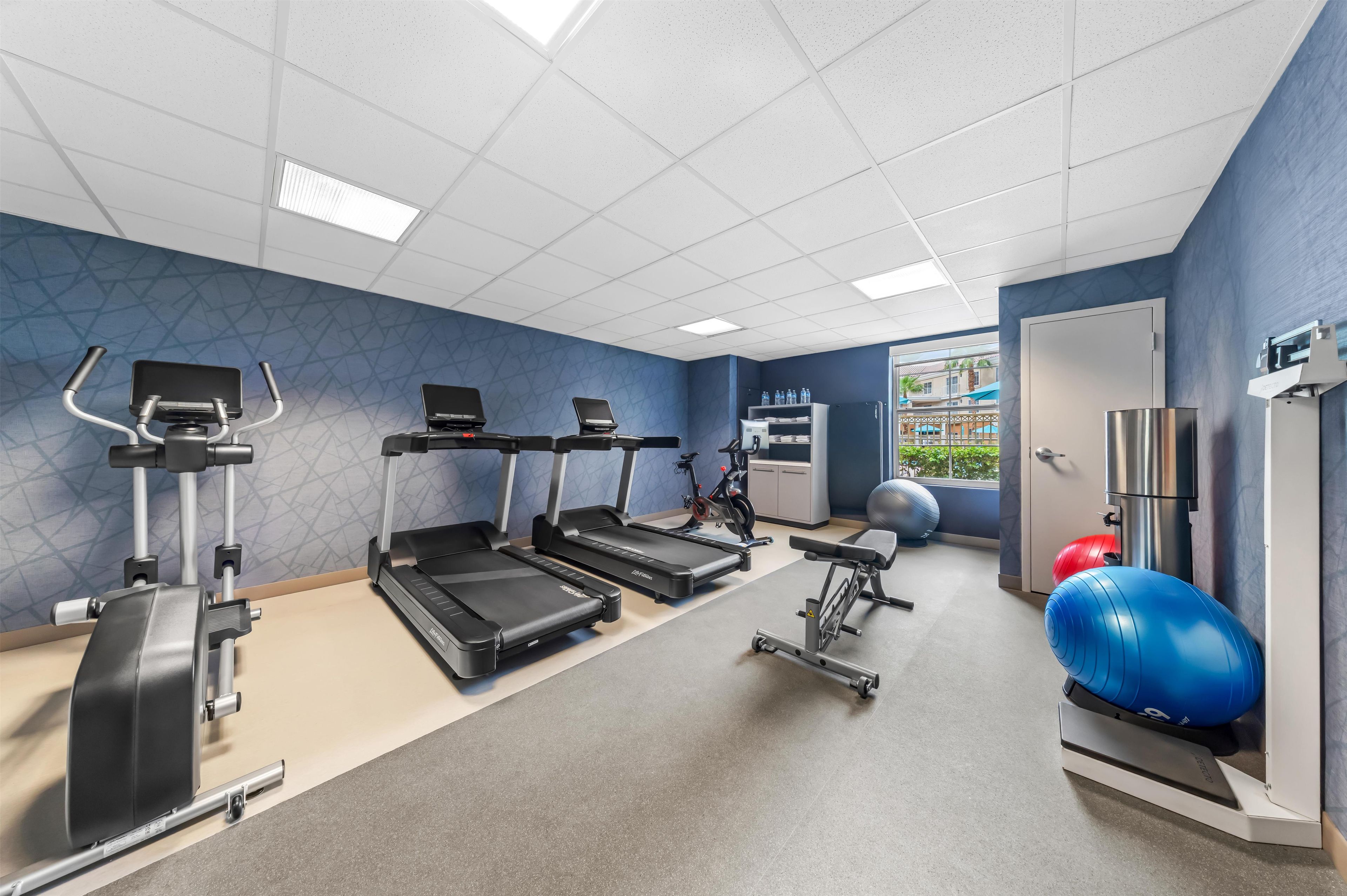 A gym with treadmills, exercise bikes, and a blue exercise ball.