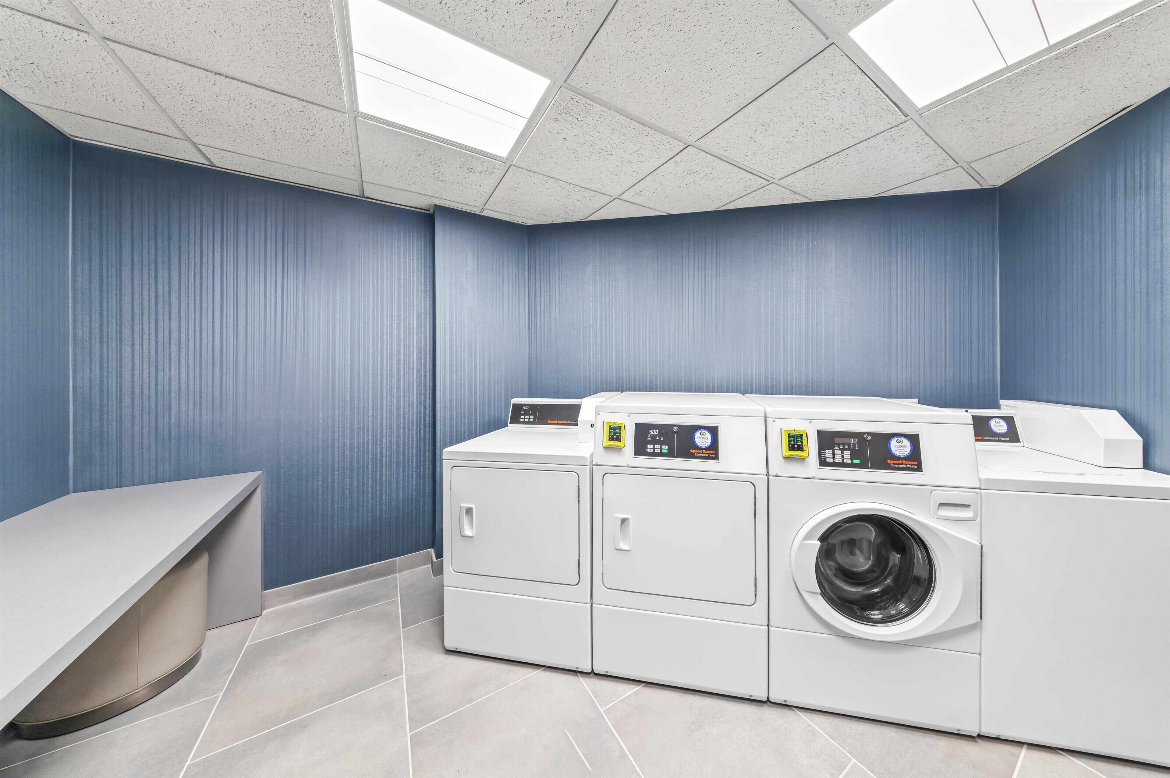 Un cuarto de lavandería con una lavadora grande, una secadora y un banco.
