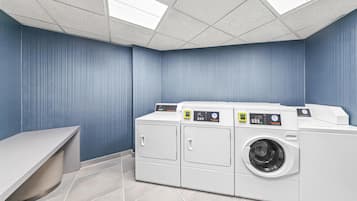 Un cuarto de lavandería con una lavadora grande, una secadora y un banco.