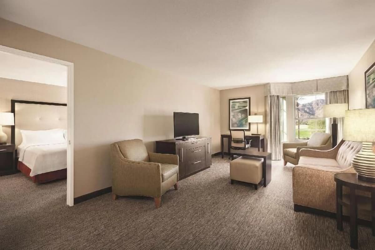 Une chambre d’hôtel comprenant un lit, deux fauteuils, un canapé, une télévision, un bureau et une fenêtre donnant sur la montagne.
