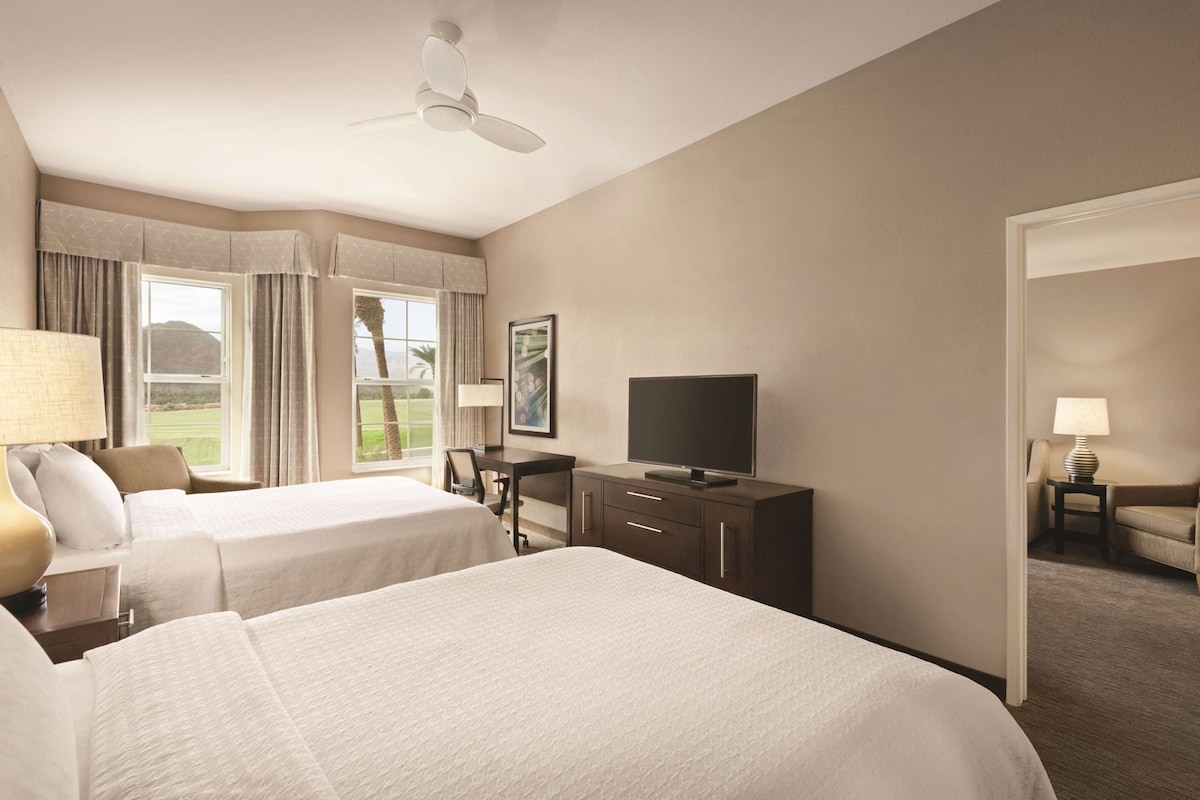 Een hotelkamer met twee bedden, een bureau, een televisie en uitzicht op een golfbaan.