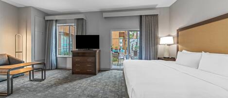 A hotel room with a bed, a TV, a desk, a chair, and a view of the outside.