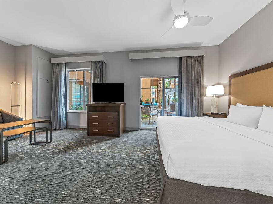 A hotel room with a bed, a TV, a desk, a chair, and a view of the outside.