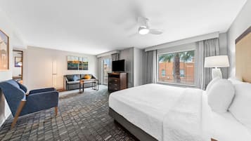 Habitación de hotel con cama, escritorio, silla, televisor y ventana con cortinas.