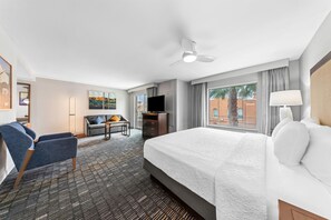 Habitación de hotel con cama, escritorio, silla, televisor y ventana con cortinas.