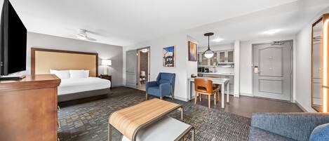 Quarto de hotel com cama, escrivaninha, cadeira e cozinha compacta.