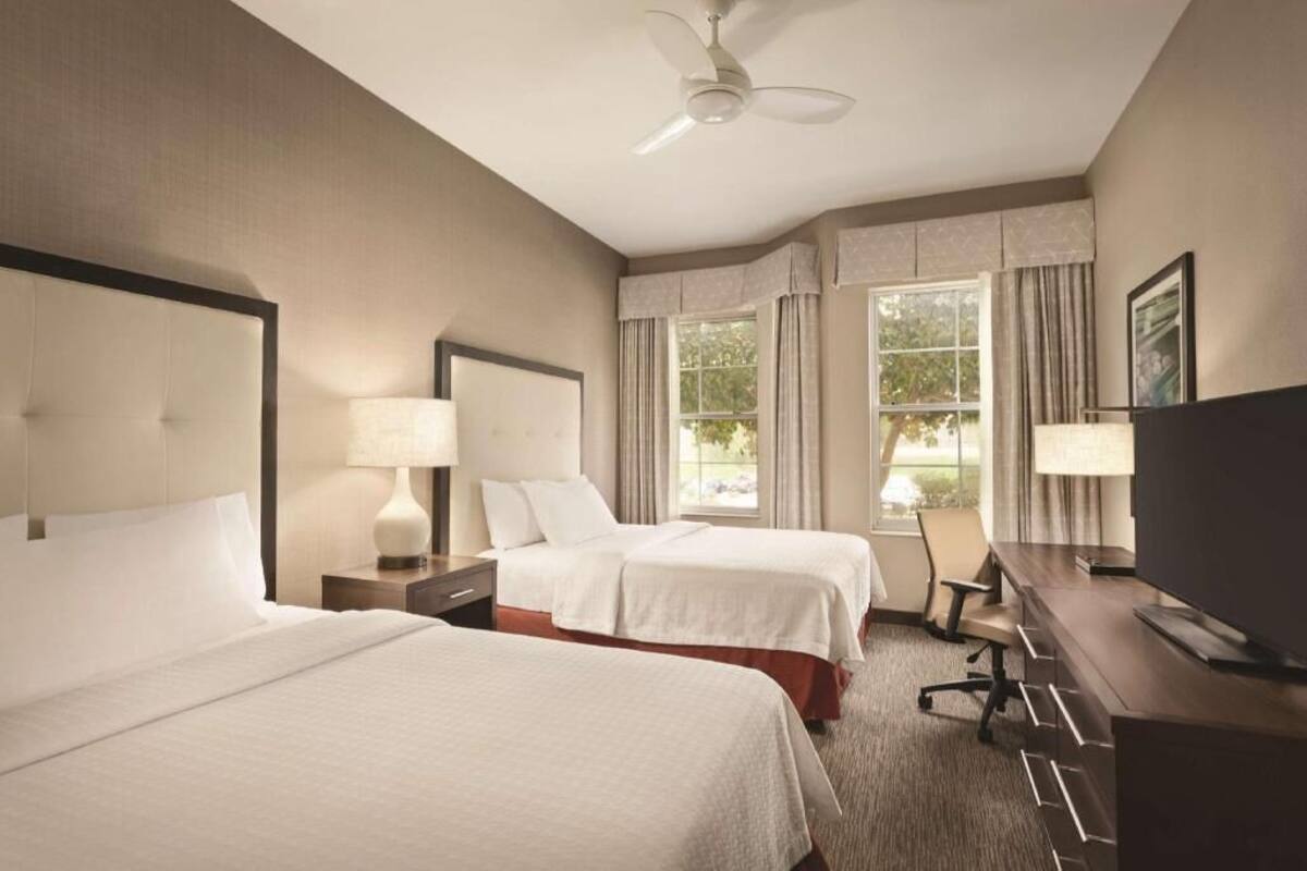 Une chambre d’hôtel avec deux lits, un bureau, une chaise, une télévision et un ventilateur de plafond.