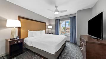 A hotel room with a bed, a desk, a TV, a ceiling fan, and a window with curtains.