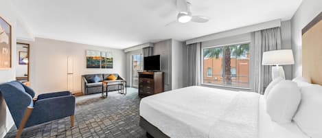 A hotel room with a large bed, a desk, a chair, a TV, and a view of the outside.