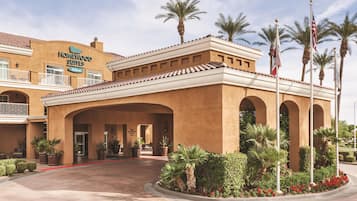 Un hotel con un letrero que dice 'Homewood Suites Hilton', que cuenta con un patio con palmeras y plantas en macetas.