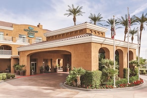 A hotel with a sign reading 'Homewood Suites Hilton,' featuring a courtyard with palm trees and potted plants.