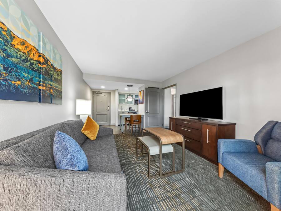 A hotel room with a sofa, a chair, a TV, a desk, and a painting on the wall.
