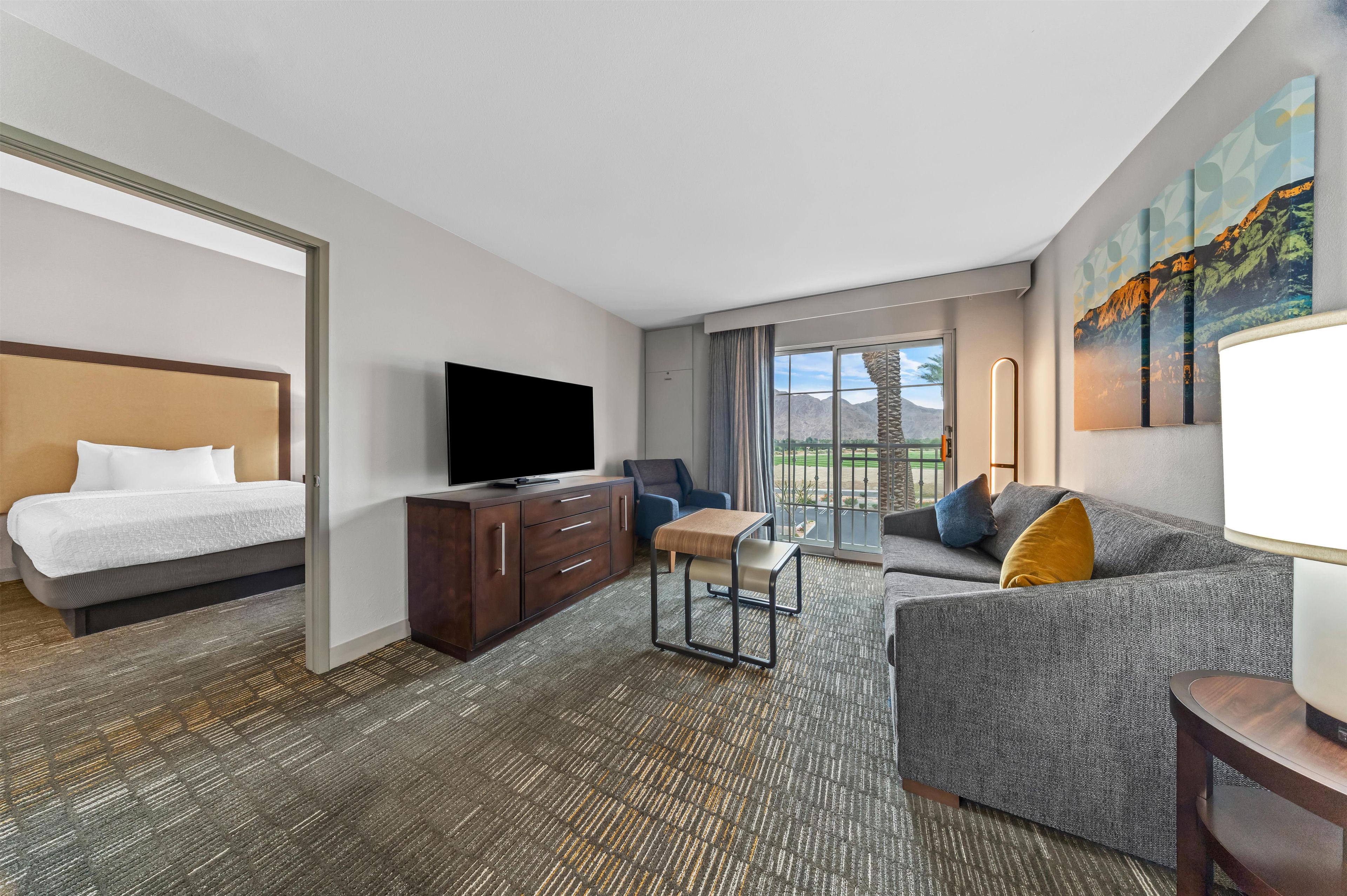 Een hotelkamer met een bed, een televisie, een bank, een bureau en uitzicht op het omliggende landschap.