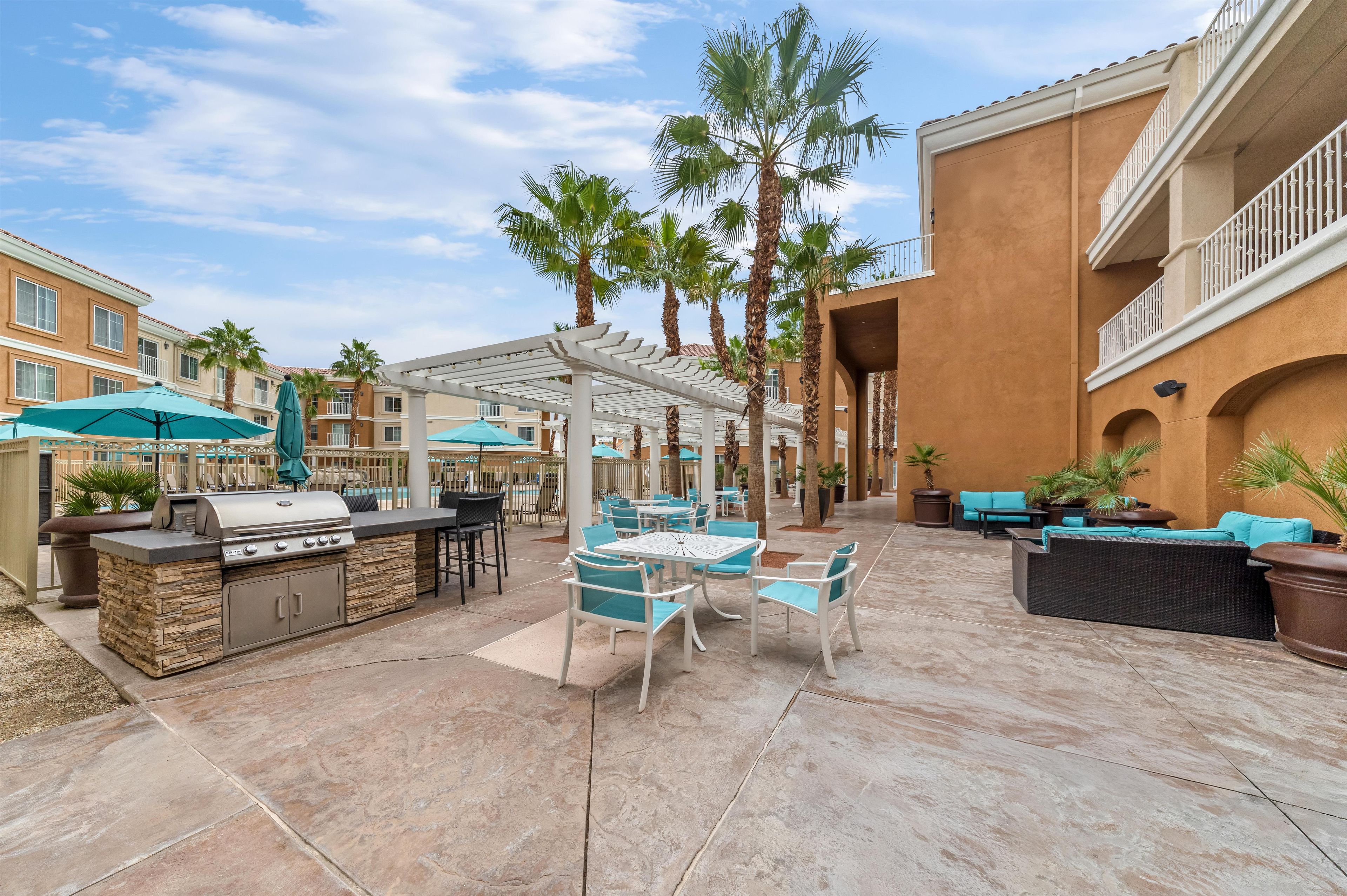 An outdoor patio area with a barbecue station, seating arrangements, and palm trees.