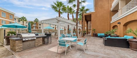An outdoor patio area with a barbecue station, seating arrangements, and palm trees.