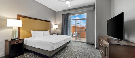 Una habitación de hotel con una cama, dos lámparas de noche, un televisor, un ventilador de techo y vistas al exterior a través de una puerta corrediza.