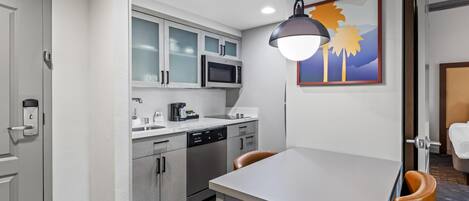 A compact kitchen with a microwave, coffee maker, and dishwasher. There is a dining table with chairs and a pendant light.