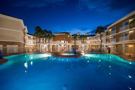 A hotel with a swimming pool, multiple balconies, and palm trees.