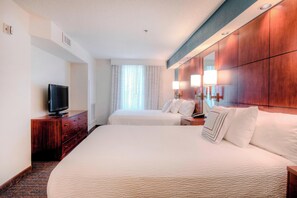 Habitación de hotel con dos camas, un televisor sobre un aparador de madera y un espejo grande en la pared.