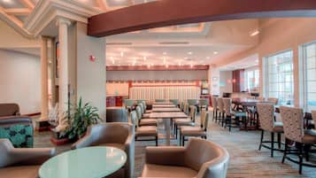 Een ruime hotel lobby met een bar in het midden, diverse zithoeken en grote ramen die zorgen voor veel daglicht.