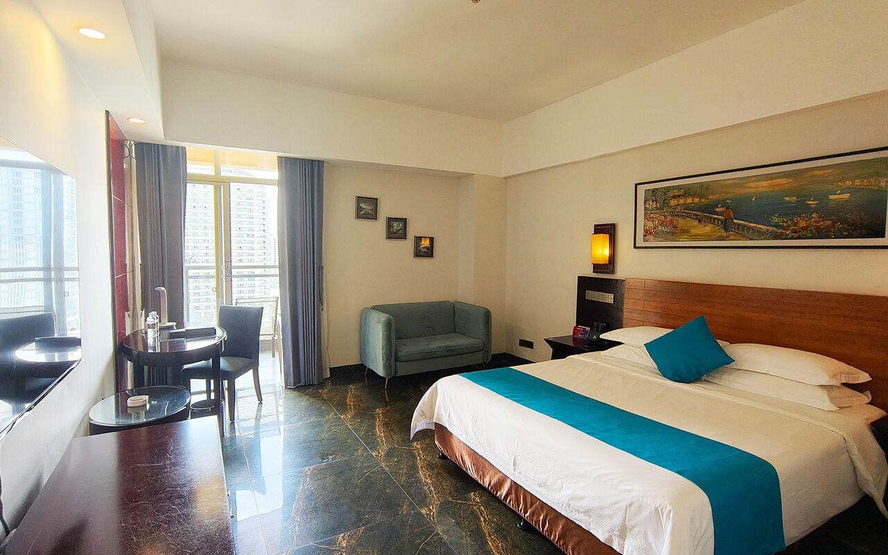 A hotel room with a bed, a desk, a chair, and a painting on the wall.
