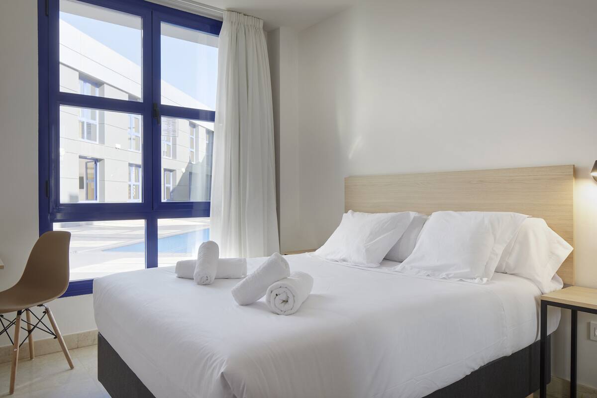 A hotel room with a large bed, a chair, a nightstand, and a window with curtains.