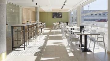 Un restaurante moderno con una barra alargada, sillas blancas y un amplio ventanal con vista a la calle.