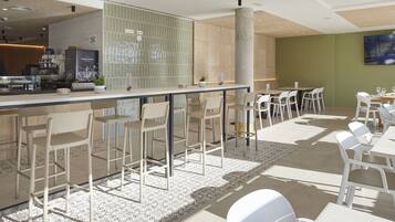 Un bar moderno con una barra larga, varios taburetes y un área de estar con mesas y sillas.