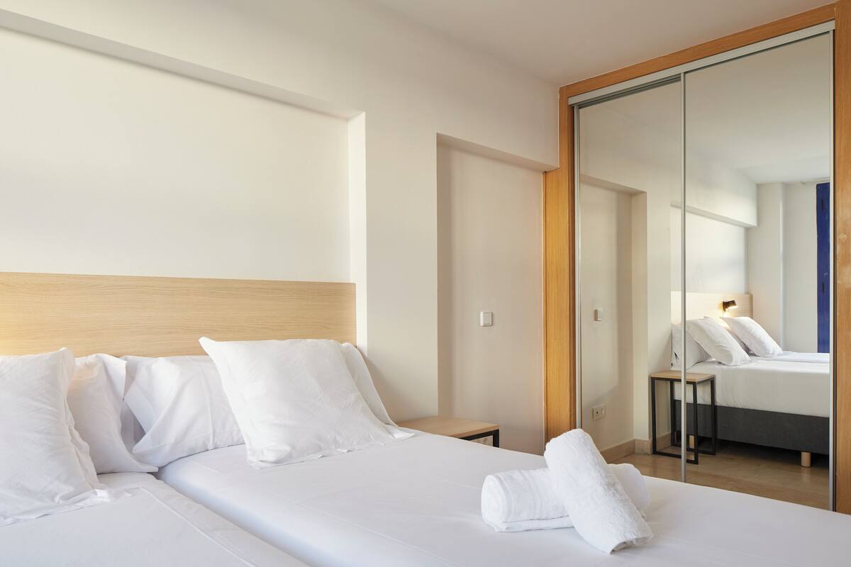 A hotel room with a large bed, a bedside table, a mirror, and a wooden headboard.