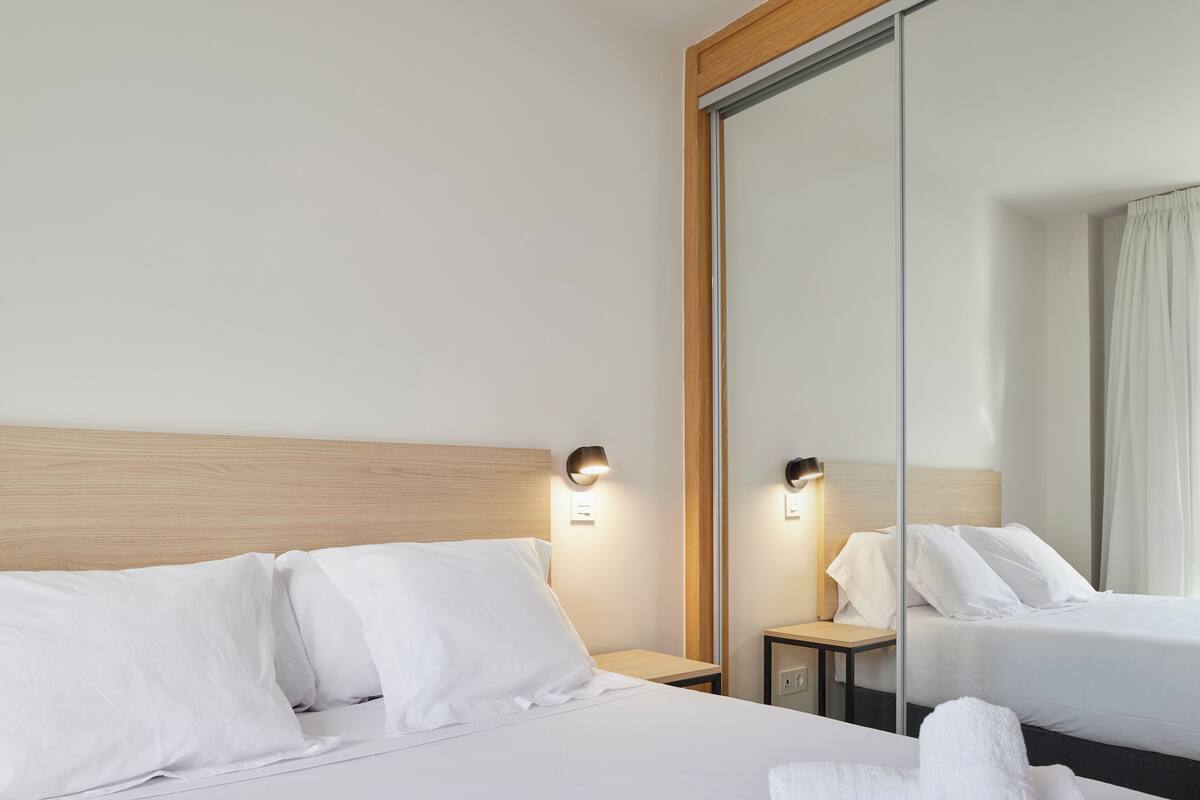 A hotel room with a wooden headboard, two bedside tables with lamps, a large mirror, and a bed with white linens.